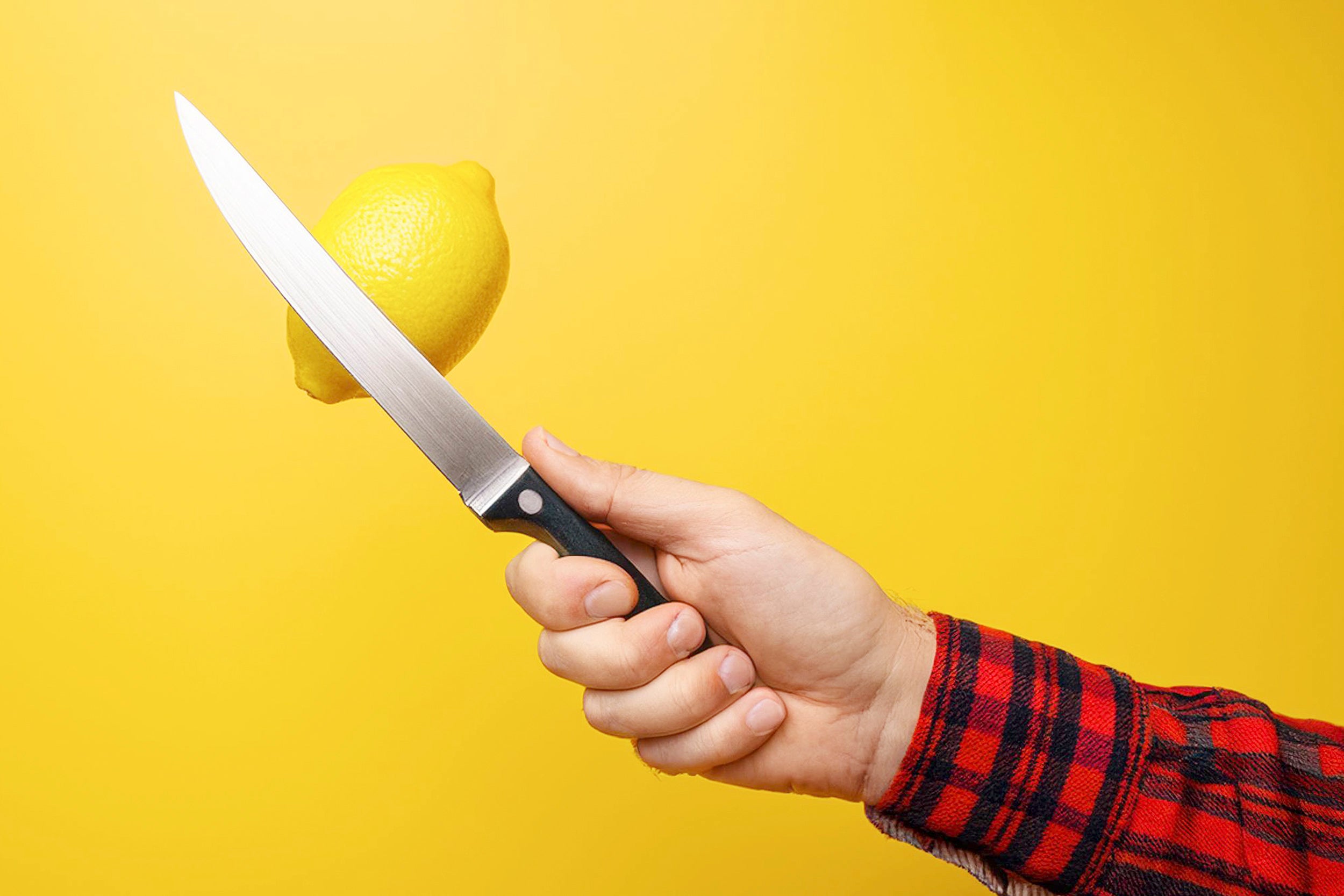 Eine Hand hält ein Messer neben einer Zitrone. Symbolisch für die Arbeitsintegration und deren Handwerk.